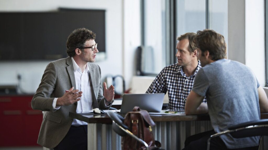 A man explaining a point with his hands while two colleagues listen in a meeting