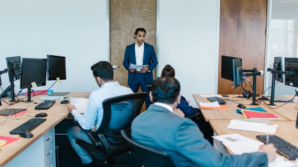 Employees working at desks in an Indian office while a manager stands nearby